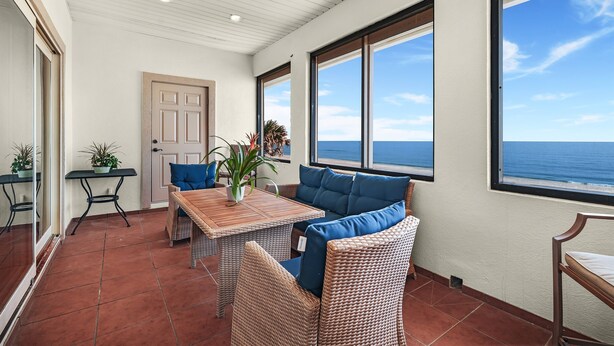 A room with a view of the sea, a wooden table, wicker furniture, and a door.
