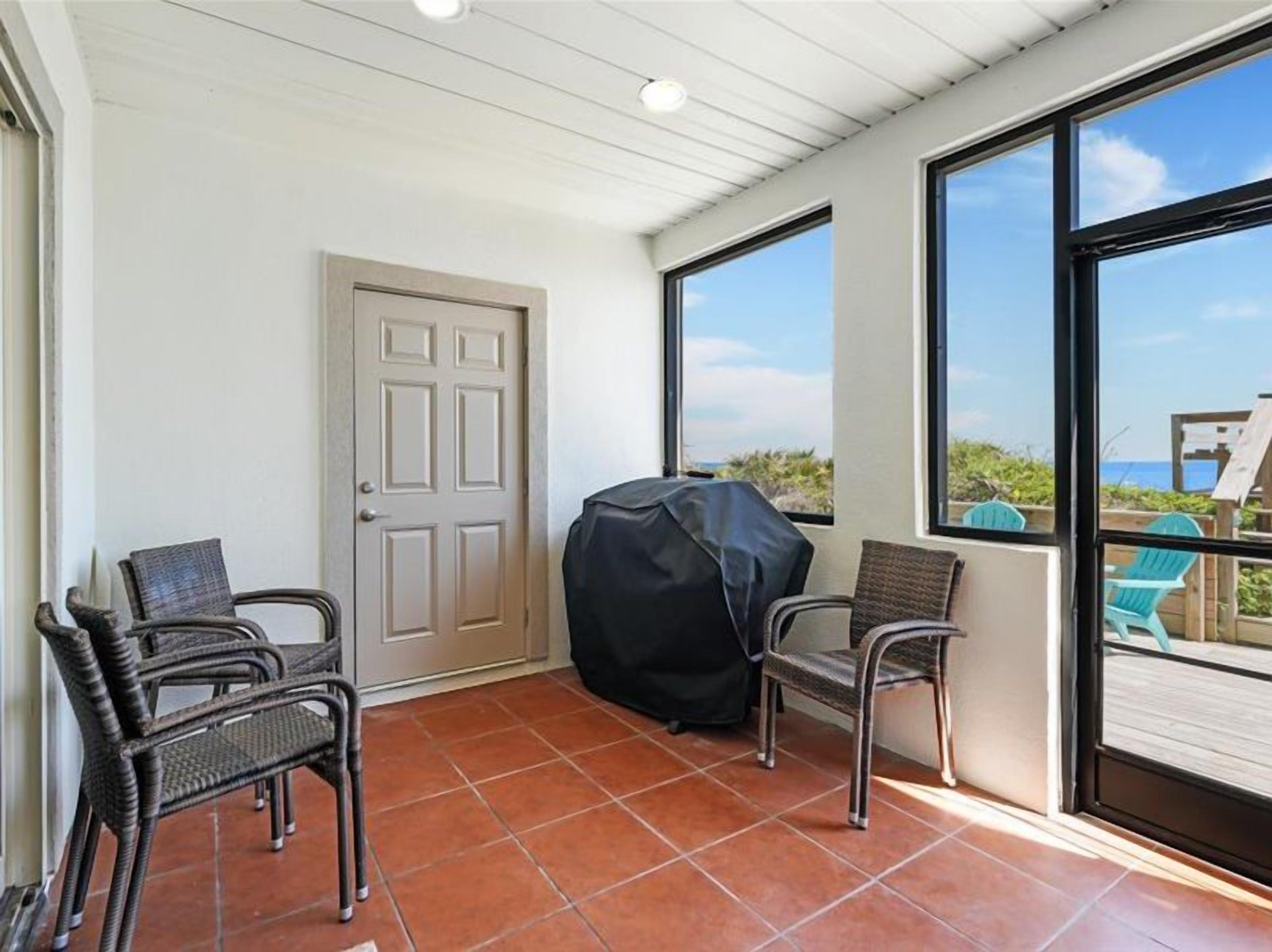 Un patio couvert comprenant deux fauteuils en osier, un barbecue et une porte.