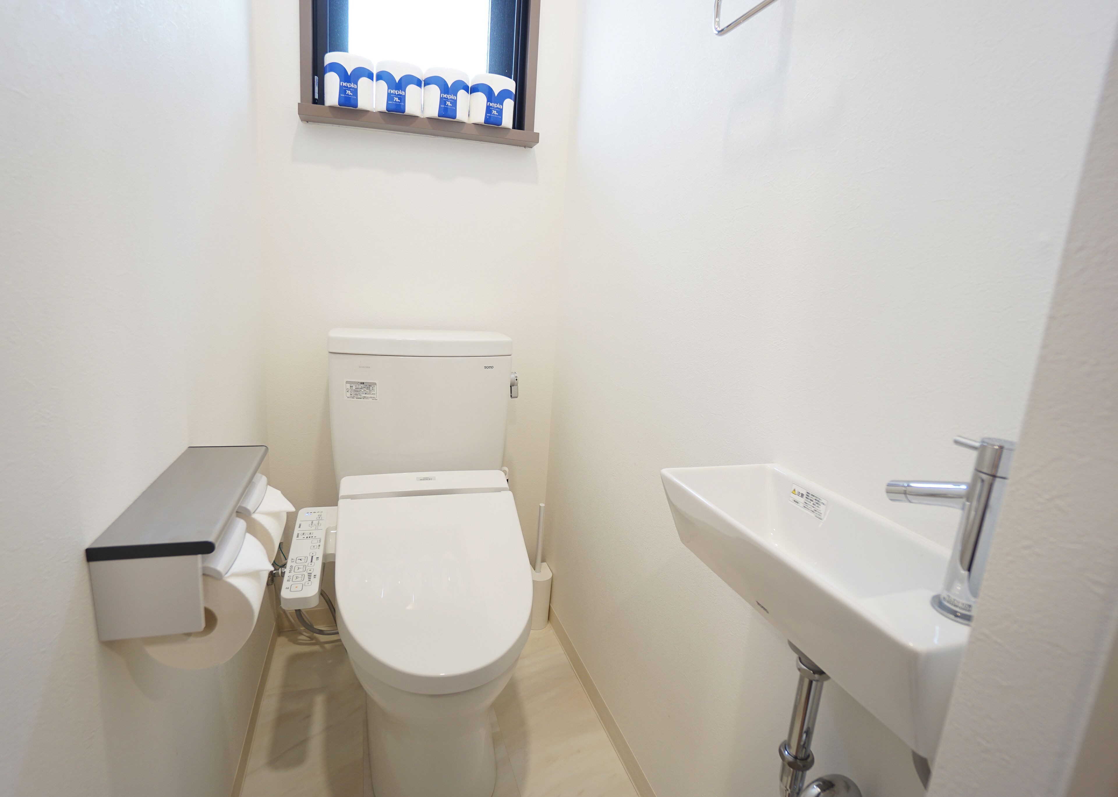 A small, white bathroom with a toilet, a sink, and a window above the toilet.