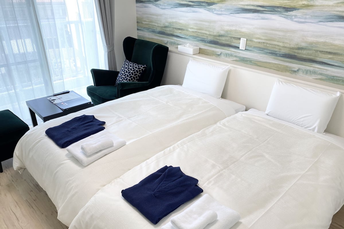 A hotel room with two beds, a desk, a chair, and a painting on the wall.