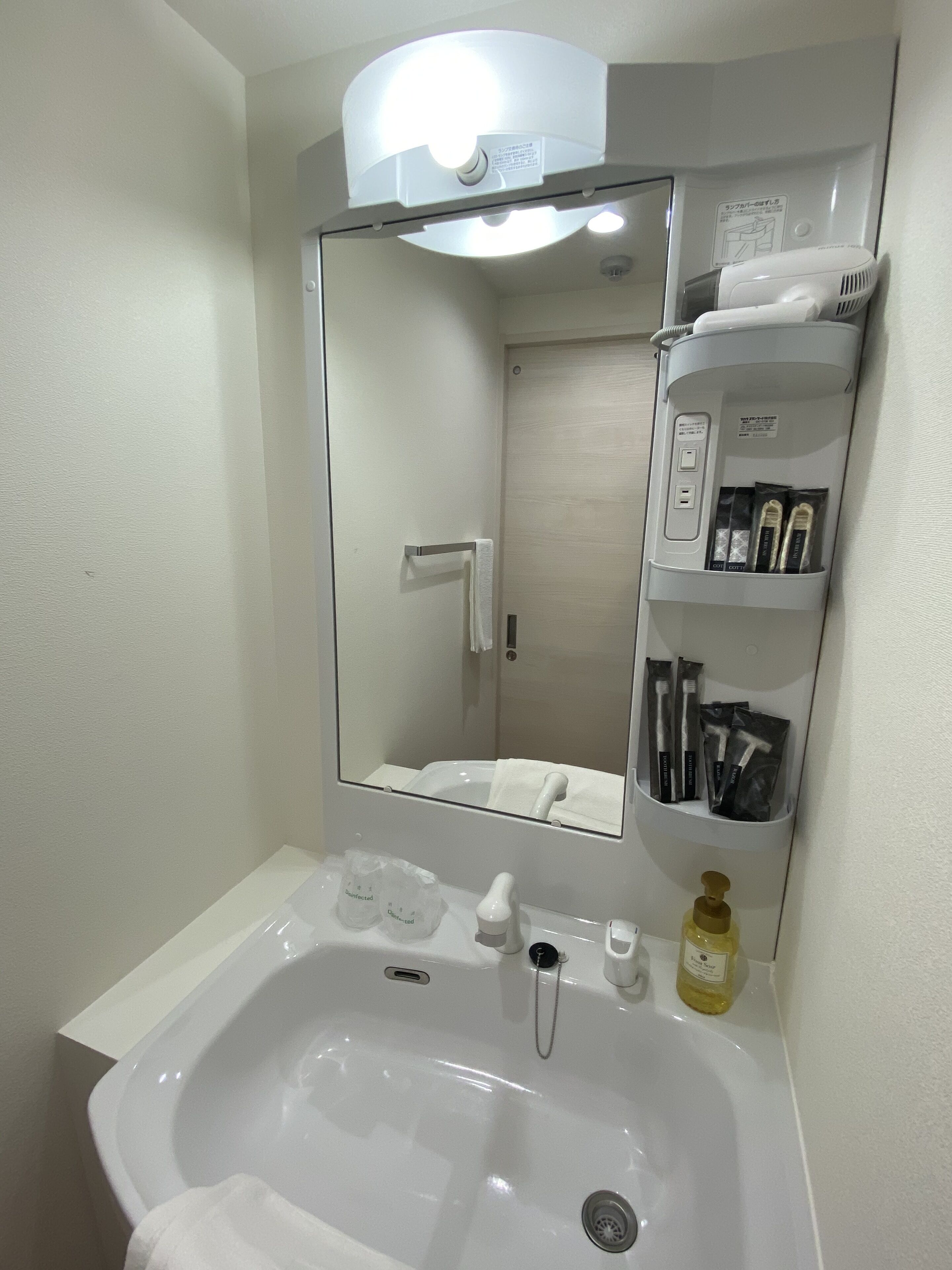 Een badkamer met een wit wastafelmeubel, een spiegel, een handdoekhouder, een zeepdispenser en een plank met toiletartikelen.