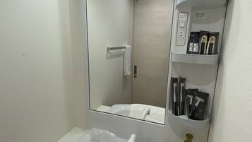 A bathroom with a white sink, a mirror, a towel rack, a soap dispenser, and a shelf with toiletries.