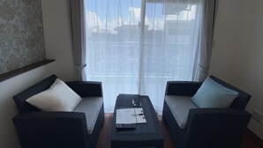 A room with two dark wicker sofas, a small table with papers, and a large window with sheer curtains. - HOTEL Ishigakijima 2020 (Ishigaki)