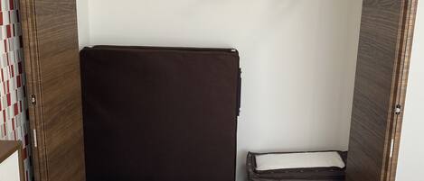 A compact room with a bed, a small storage unit, and a hanging clothes rack.