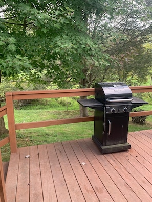 A barbecue grill on a wooden deck with a wooden railing.