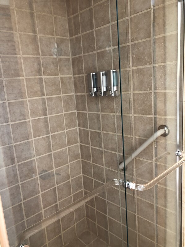 Un área de ducha con paredes de azulejos, una puerta de cristal y una barandilla.