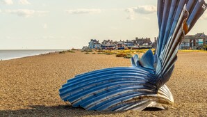 Una gran escultura metálica en la playa, con edificios al fondo.
