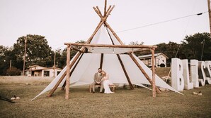 Ein Teepee aus Holz mit weißem Canvas-Zelt, einer Bank und dem Wort "BLESSED" in großen Buchstaben.