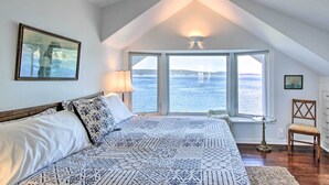 A bedroom with a large bed, a ceiling fan, a window with a view of the sea, and a small table with a chair. - Fire Pit, Views & Beach Access: Waterfront Escape! (University Place)
