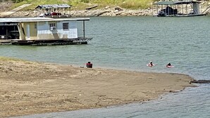 Een drijvend huis met een steiger, een zandstrand en een rustig waterlichaam.