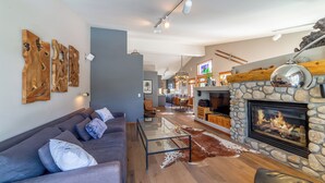 A modern living room with a stone fireplace, a gray sofa, and wooden wall art. - Luxurious Golf Front Home Mountain Views 479 (Mammoth Lakes)