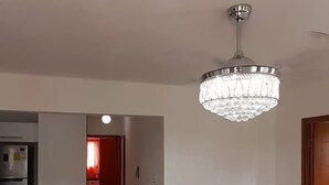 A modern living room with a glass-top coffee table, a chandelier, and a kitchen area in the background. - Residencial Don Mero (La Vega)