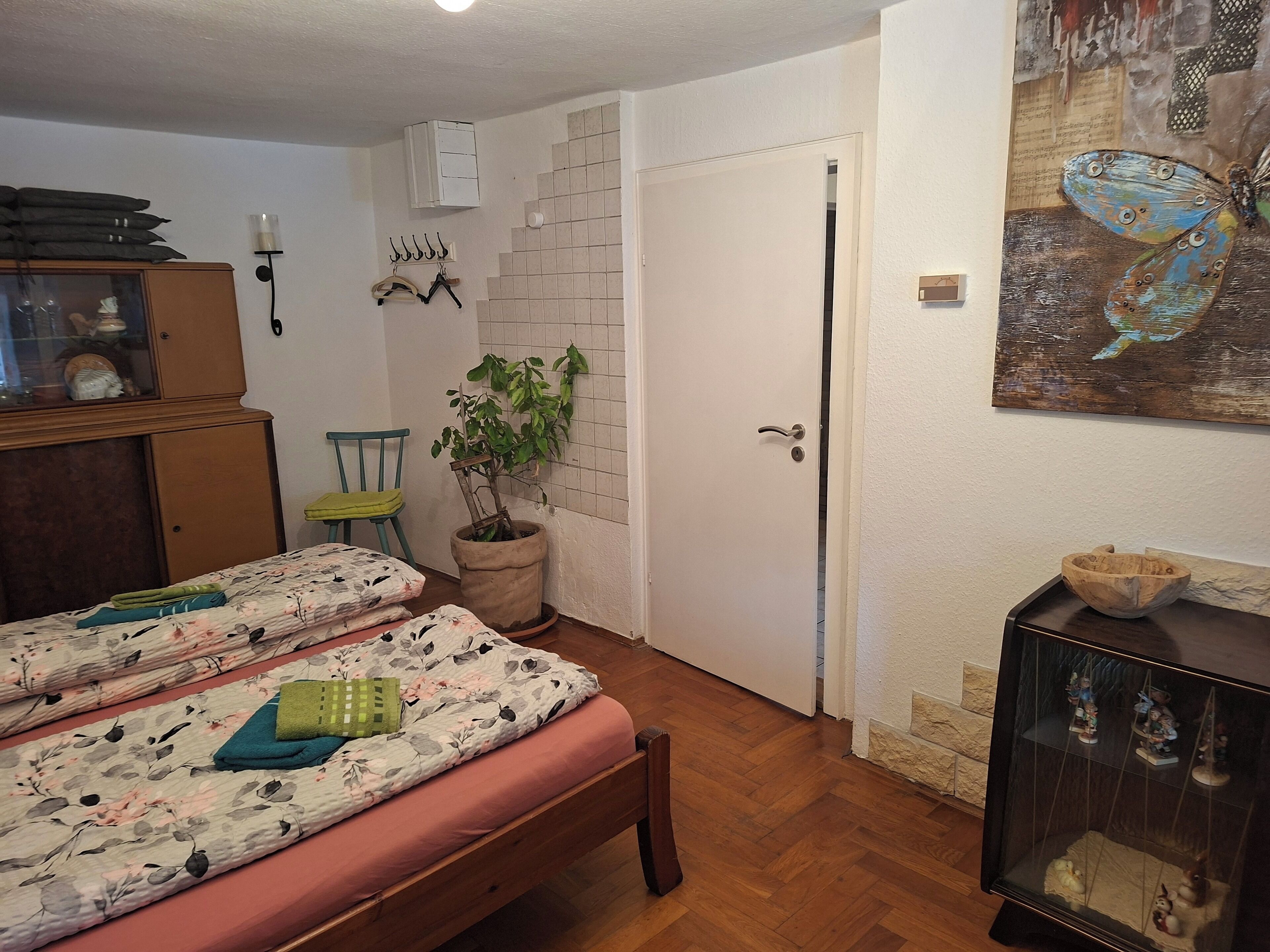 Una habitación con dos camas, una planta en maceta, un aparador de madera y una repisa con figuritas.
