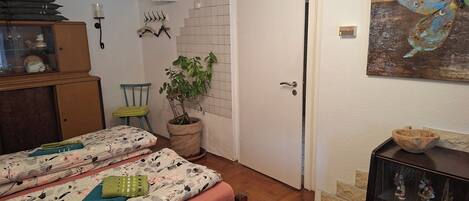 Una habitación con dos camas, una planta en maceta, un aparador de madera y una repisa con figuritas.