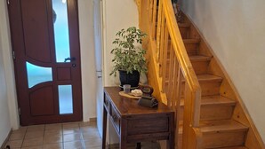 Un escalier avec des rampes en bois menant à l’étage supérieur, une plante en pot posée sur une petite table et une porte dotée d’un panneau en verre dépoli.