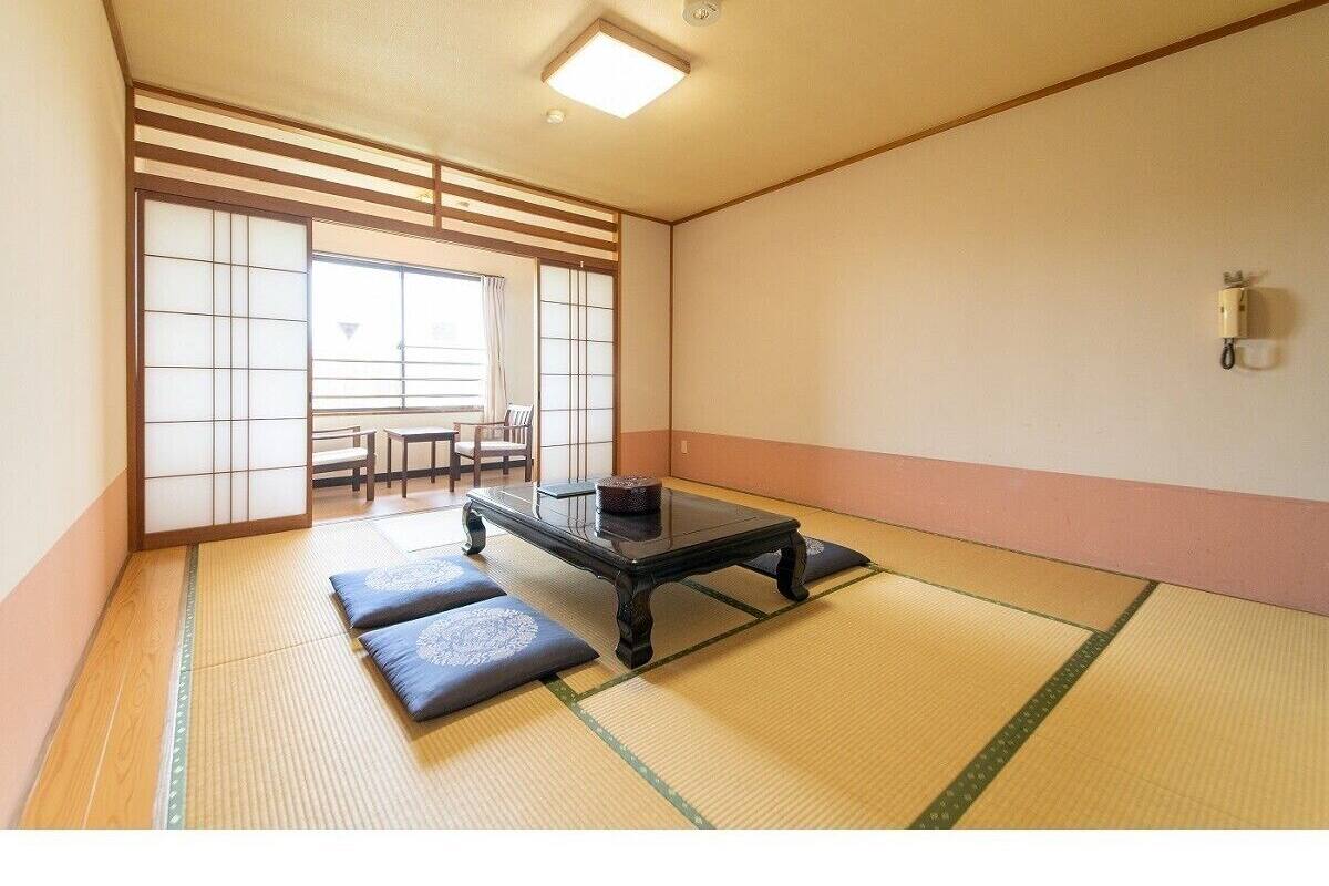 A tatami mat room with a low table and cushions, a sliding door, and a view of a traditional Japanese room.