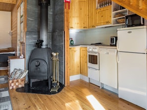 Une cuisine chaleureuse, aménagée dans le style d’un chalet, avec un poêle à bois, des armoires en bois et un réfrigérateur blanc.