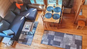 A cozy cabin interior with a sofa, a dining table, and a large window.