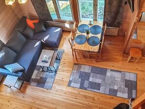 L’intérieur d’un chalet chaleureux, avec un canapé, une table à manger et une grande fenêtre.