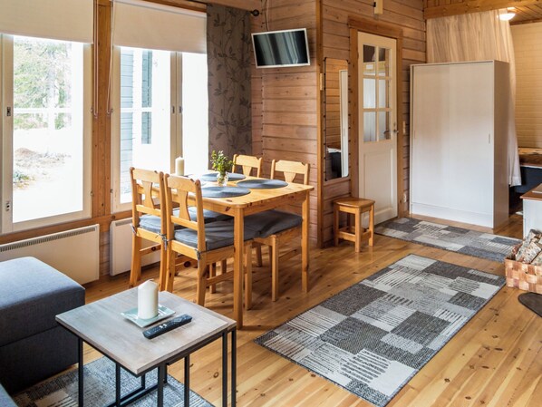 A wooden cabin interior with a dining table, chairs, a TV mounted on the wall, and a cozy seating area. - Yllästokka 5 by Interhome (Ylläsjärvi)