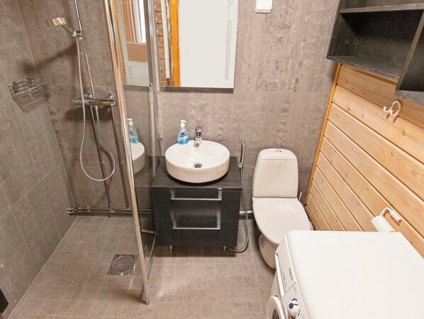 A compact bathroom with a shower, sink, toilet, and a wooden vanity.