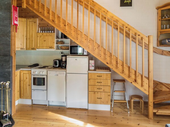 Een keuken met houten kasten, een magnetron, een koelkast en een houten trap.