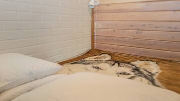 Ein Zimmer mit weißen Ziegelwänden, Holzvertäfelung, einem Bett mit weißer Bettwäsche und einer wandmontierten Leuchte.