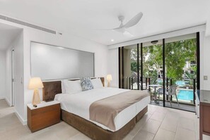 A modern hotel room with a large bed, a ceiling fan, a view of a swimming pool, and a balcony.