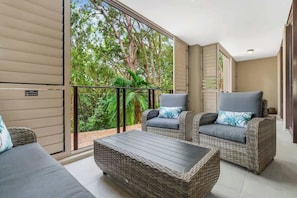 A balcony with wicker furniture, a view of trees, and a door to the right.
