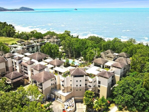 A resort with multiple buildings, a swimming pool, and a view of the ocean.