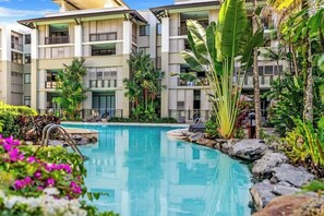 A hotel with a swimming pool surrounded by tropical plants and a multi-story building with balconies.