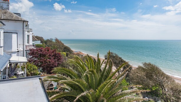 Blick auf die Küste mit Strand, einem weißen Gebäude mit Balkon und üppiger Vegetation.