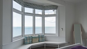 Ein Schlafzimmer mit Erkerfenster mit Meerblick, einer weißen Bank mit Kissen und einem Spiegel an der Wand.