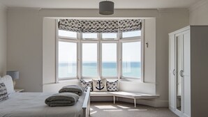 Ein Schlafzimmer mit einem großen Erkerfenster, einem Bett mit Kissen, einer Bank und einem Kleiderschrank.