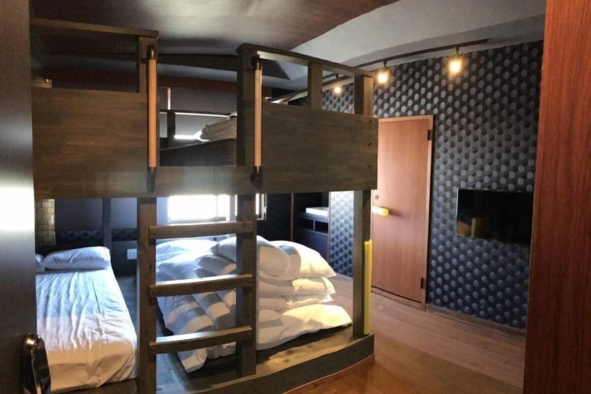 Dormitorio con literas, una escalera de madera, una puerta y un papel pintado.