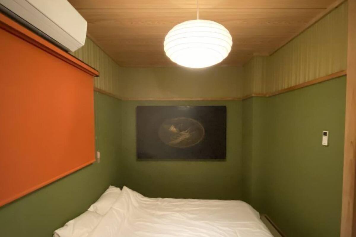 Una habitación pequeña con cama individual, paredes verdes, techo de madera y cama blanca.