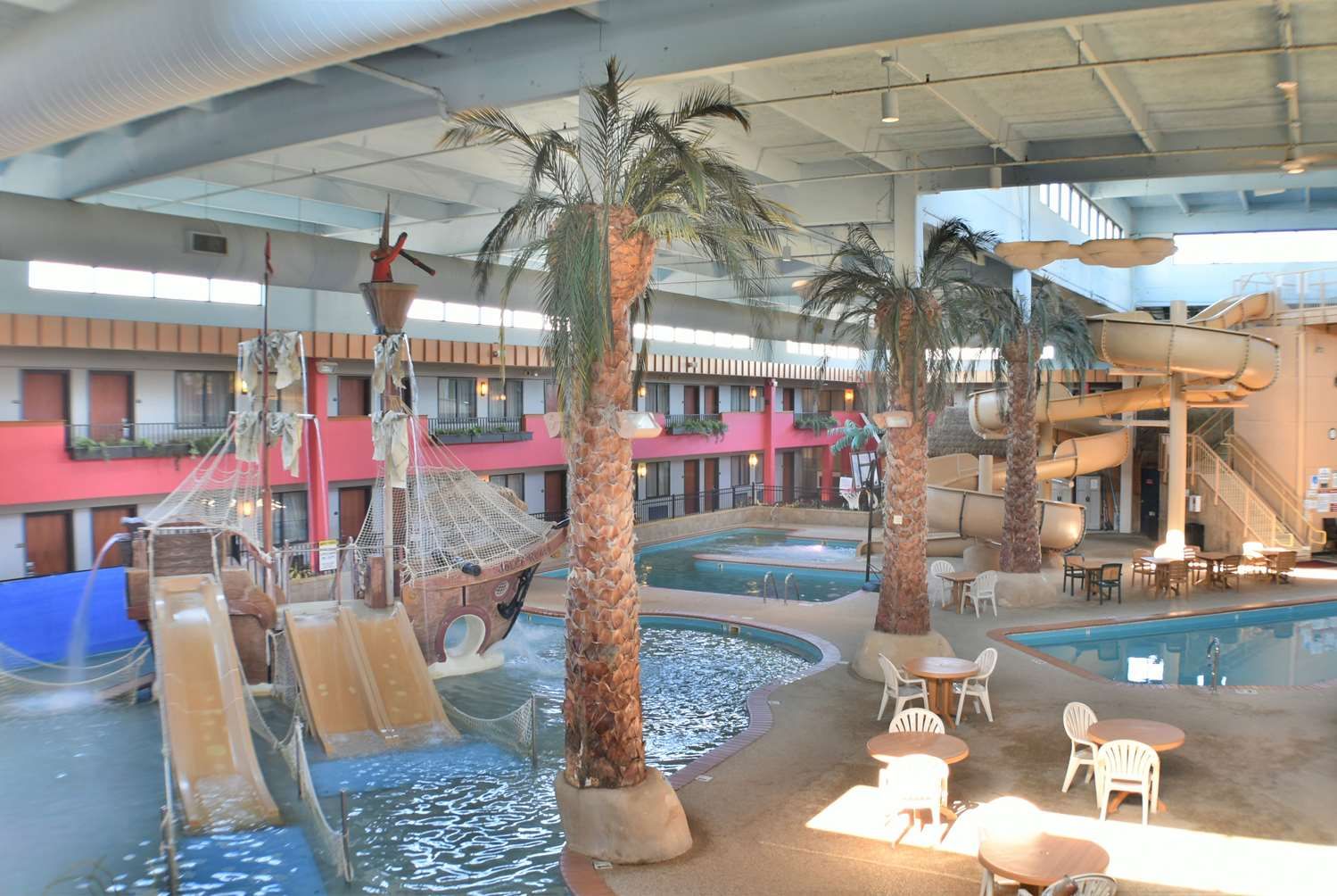 An indoor pool area with slides, palm trees, and lounge seating.
