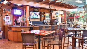 Un restaurante con zona de bar, sillas de mimbre y mesas.