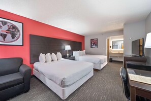 A hotel room with two beds, a desk, a chair, a TV, and a red accent wall. - Ramada by Wyndham Sioux Falls Arpt & Suites (Sioux Falls)