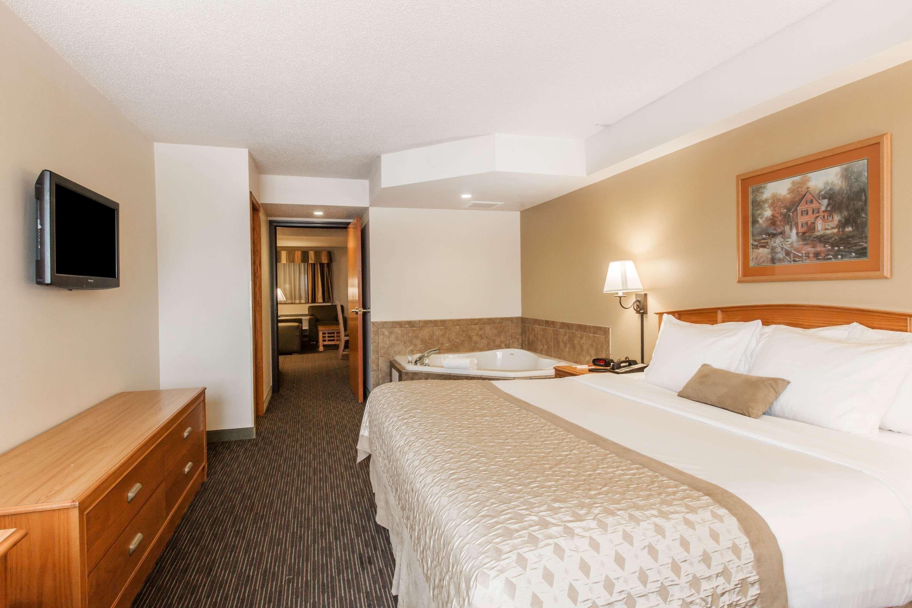 A hotel room with a bed, a TV, a desk, a lamp, and a painting on the wall.