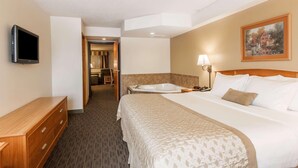 Una habitación de hotel con cama, televisión, escritorio, lámpara y un cuadro en la pared.