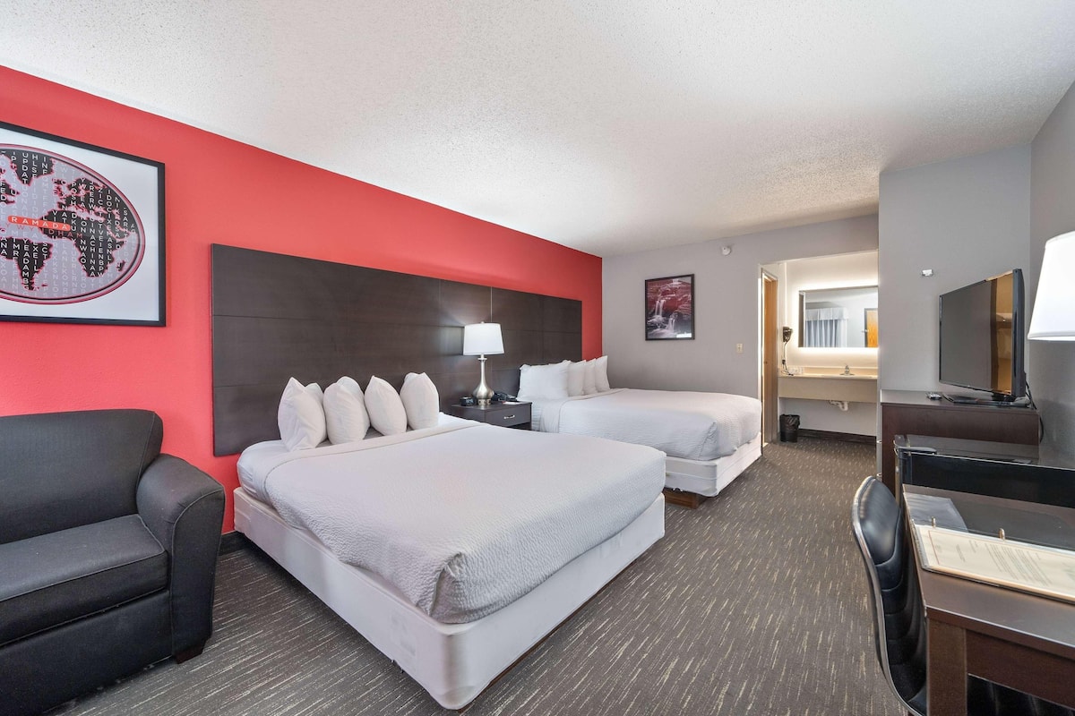 Une chambre d’hôtel avec deux lits, un bureau, une chaise, une télévision et un mur d’accent rouge.