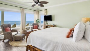 A hotel room with a large bed, a ceiling fan, a TV, and a view of the ocean.