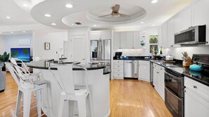 A modern kitchen with white cabinetry, stainless steel appliances, and a central island with bar stools. - Waterfront Escape—Private Pool, Game Room, Hot Tub & Dockside Views Near Indian Rocks Beach (Indian Rocks Beach)