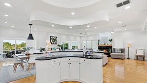 A modern kitchen with white cabinets, a curved island, and a dining area with a gray rug. - Waterfront Escape—Private Pool, Game Room, Hot Tub & Dockside Views Near Indian Rocks Beach (Indian Rocks Beach)