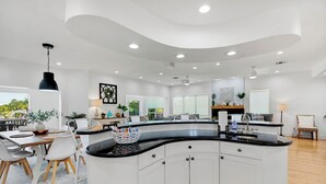 A modern kitchen with a curved island, white cabinetry, and a black countertop. - Waterfront Escape—Private Pool, Game Room, Hot Tub & Dockside Views Near Indian Rocks Beach (Indian Rocks Beach)