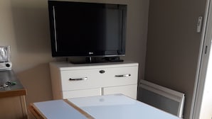Een kamer met een televisie op een kast, een tafeltje en een kast met lades.