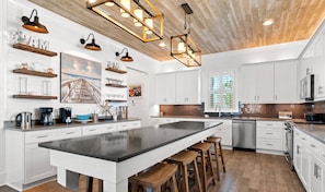 A spacious kitchen with a large island, wooden stools, white cabinetry, and pendant lighting. - 🌊 Sea Dreaming | Dog Friendly* | Golf Cart | Bikes | Arcade System ✨ (Miramar Beach)