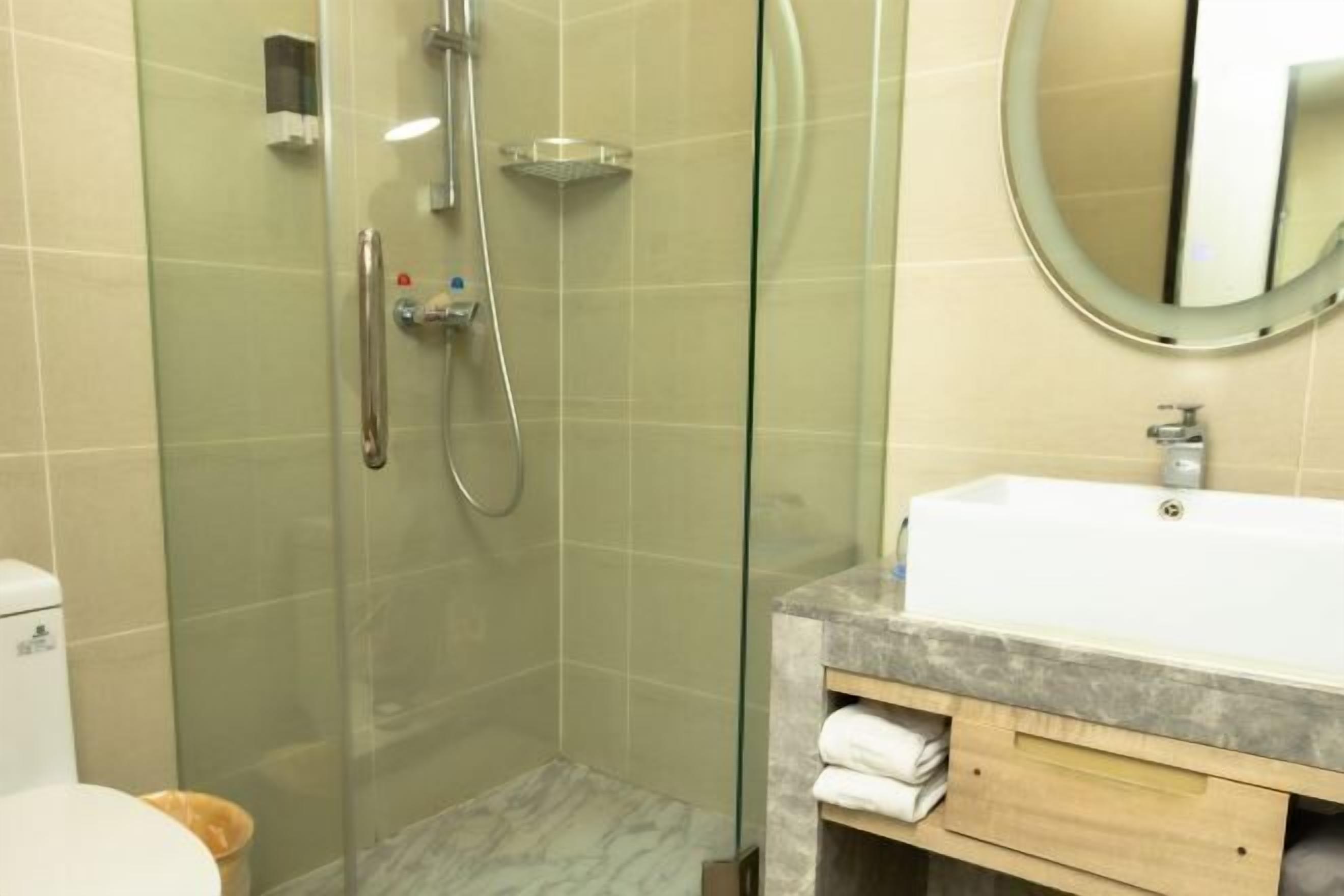 A modern bathroom with a glass-enclosed shower, a white sink with a marble countertop, and a wooden vanity.