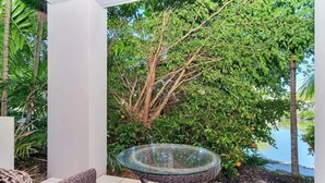 Ein Tisch mit Glasplatte und Korbstühle in einem Gartenbereich mit Blick auf einen Baum und ein Gewässer.